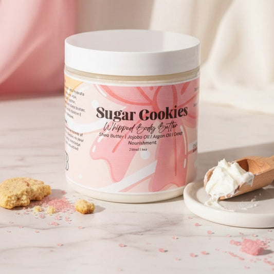 Container of 'Sugar Cookies' whipped body butter with a scoop and cookies on a light background